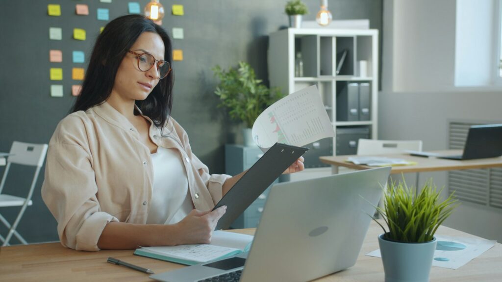 Mitarbeiterin prüft Unterlagen am Büroschreibtisch, um Prozesse in der Verwaltung zu verschlanken